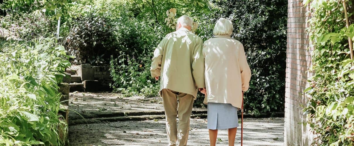 Elderly couple walking away from camera on a path surrounded by trees on either side